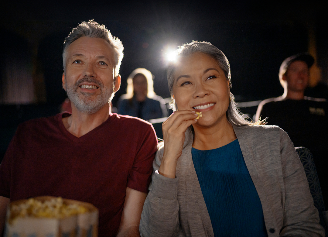 man and woman in a movie theater eating popcorn listening with LE audio and Auracast hearing aids
