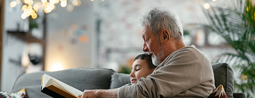 Grandfather reading a book to grandson under holiday lights